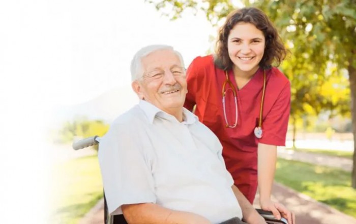 A smiling elderly man in a wheelchair with a nurse outdoors.