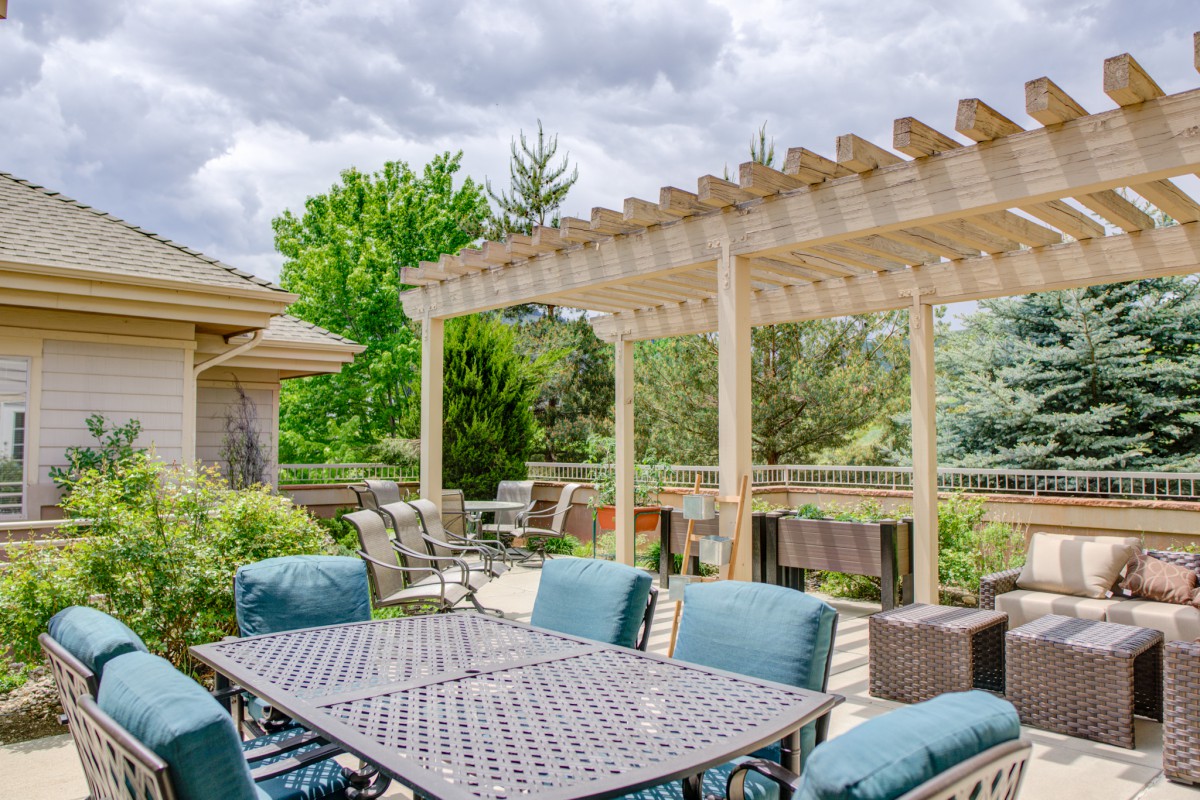 A spacious outdoor patio featuring a pergola and comfortable seating area surrounded by lush greenery.