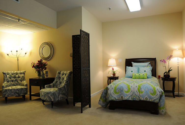 A cozy bedroom interior with a bed, chair, table, and lamp.