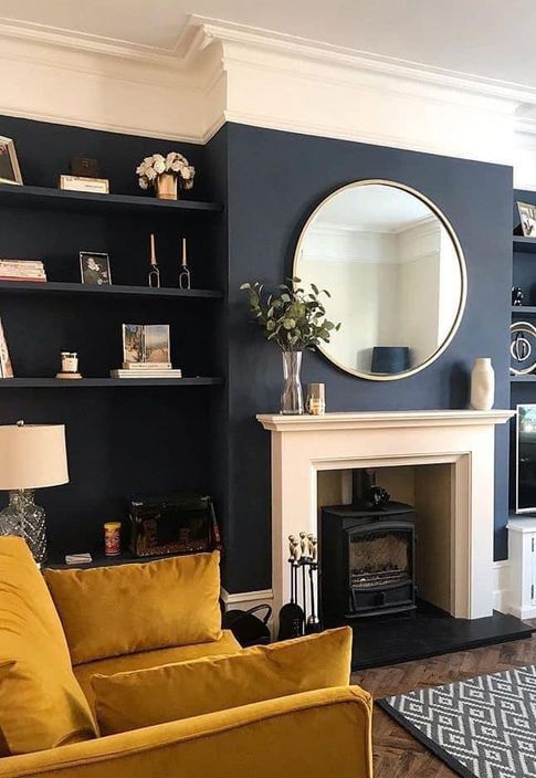 A modern living room featuring a stylish fireplace, large circular mirror, and navy blue accent wall with shelving.