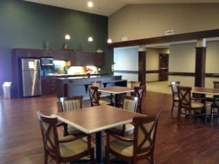 A cozy dining area with wooden tables and chairs, featuring a serving counter and ambient lighting.