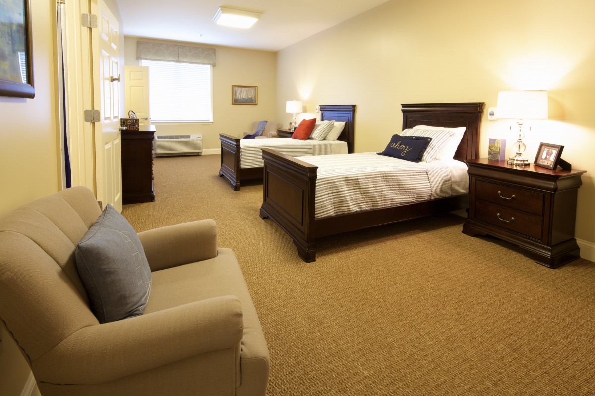 A cozy bedroom interior featuring two beds, an armchair, and warm lighting.