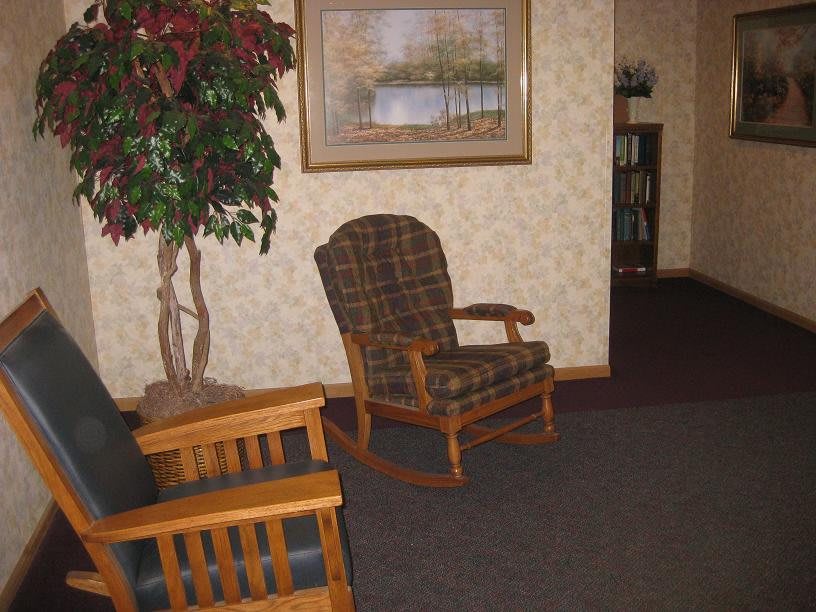 A cozy living room with a wooden rocking chair and a framed landscape painting on the wall.