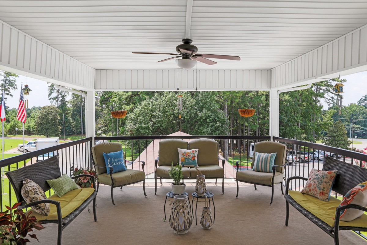 A cozy porch with comfortable seating and a ceiling fan overlooking a lush garden.
