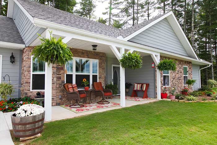 A cozy porch with comfortable seating and hanging plants, attached to a house with brick walls and a well-kept lawn.