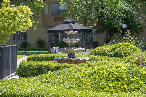 A tranquil garden featuring a beautiful fountain, surrounded by lush greenery and a gazebo.