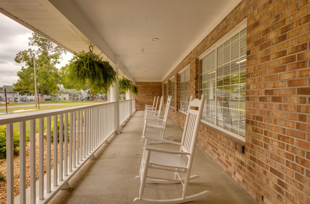 A peaceful suburban porch featuring white rocking chairs and hanging plants.