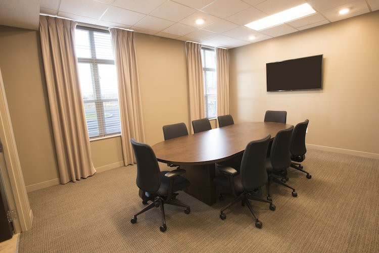 A modern conference room with a large table and chairs, featuring windows and a wall-mounted television.