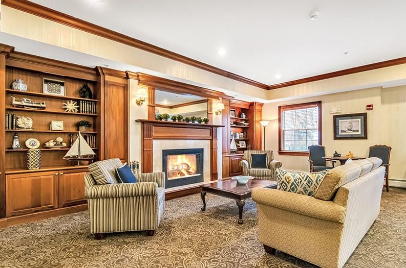 A cozy living room with a fireplace, surrounded by comfortable furniture and wooden shelves.