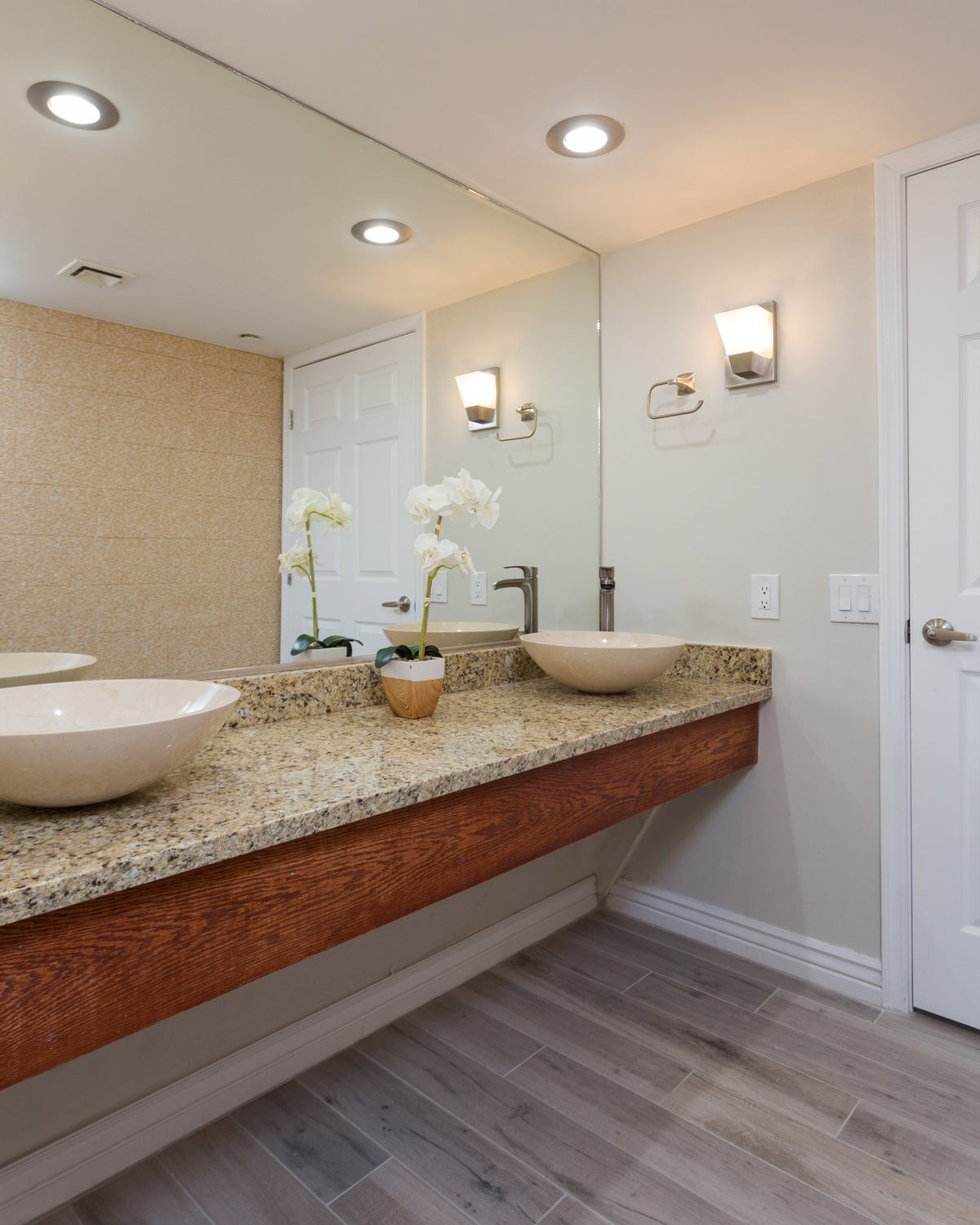 A modern bathroom featuring double vessel sinks on a granite countertop with wall-mounted mirrors and contemporary lighting fixtures.