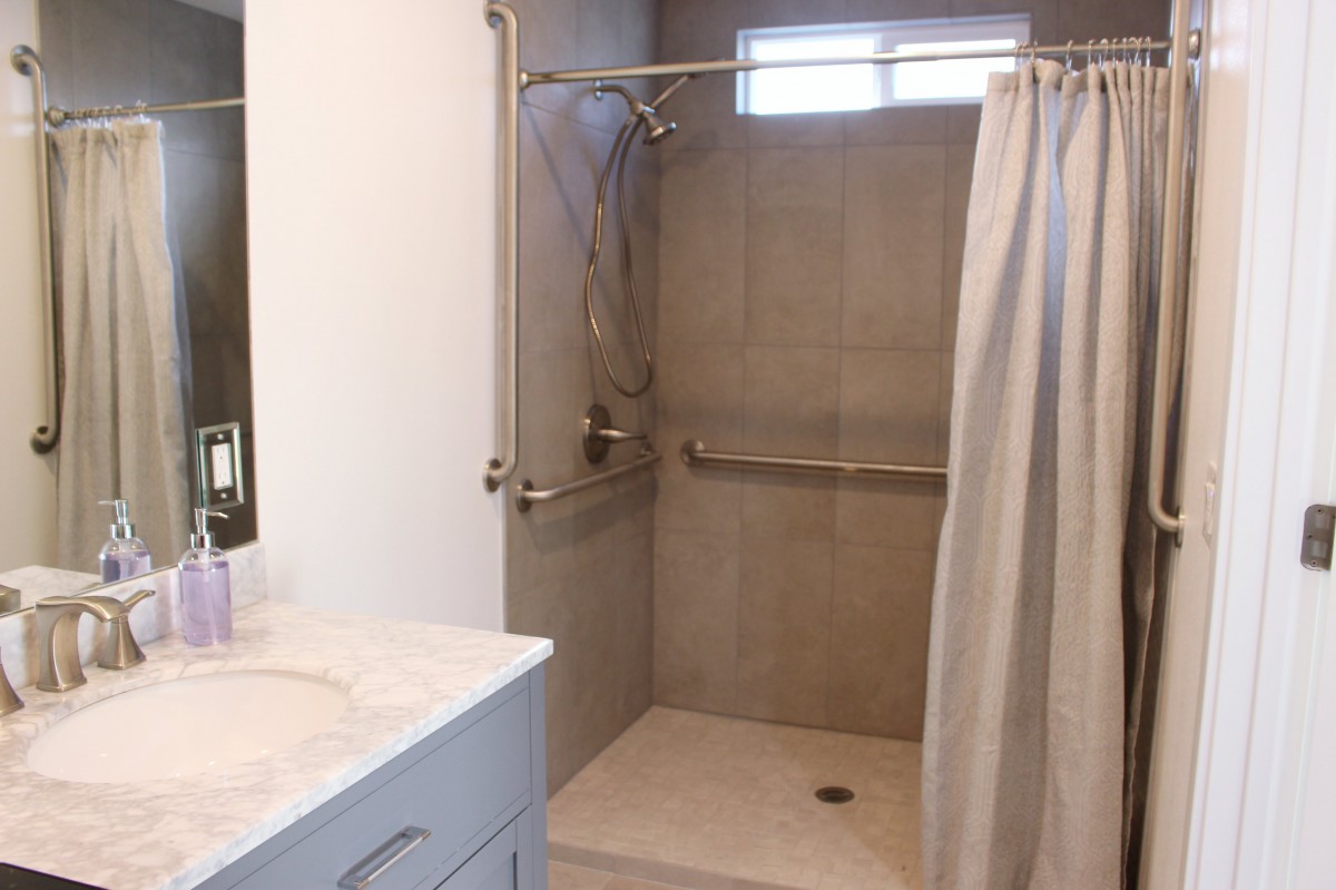 A bathroom featuring a tiled shower with grab bars and a curtain, adjacent to a sink.