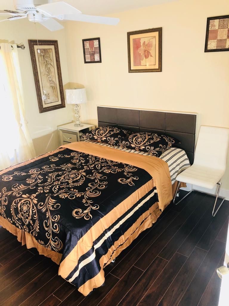 A neatly arranged bedroom featuring a stylish bed with patterned bedding, artwork on the walls, and a modern lamp on a side table.