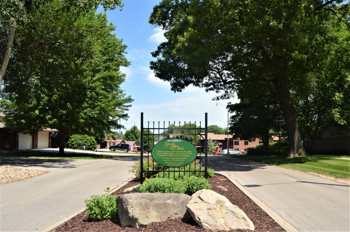 Entrance sign surrounded by trees and greenery on a sunny day.