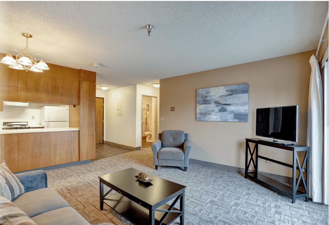A modern living room with neutral colors, featuring a comfortable armchair, a coffee table, and a television.