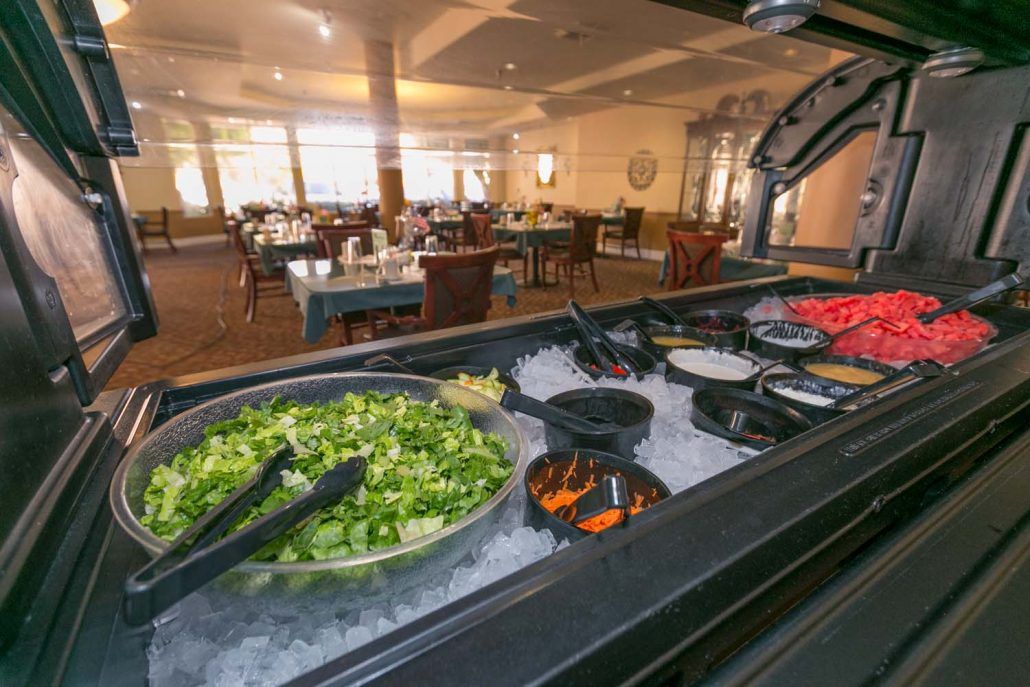 A salad bar in a spacious restaurant setting, featuring various fresh vegetables.
