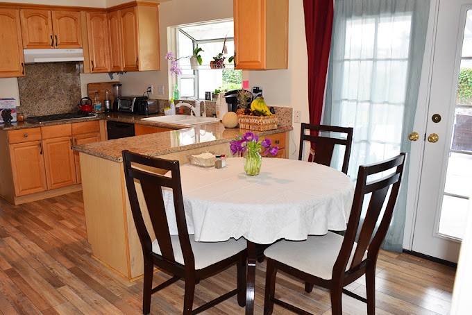 A cozy dining area with a round table covered by a white tablecloth, surrounded by wooden chairs, adjacent to a modern kitchen.