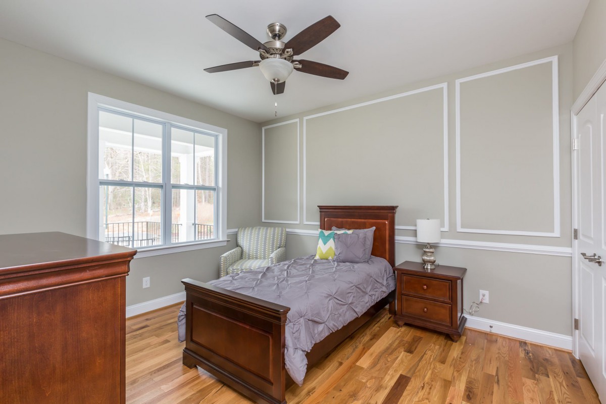 A cozy bedroom with a single wooden bed, hardwood floors, and a ceiling fan.