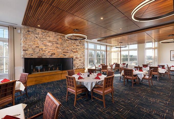 An elegant dining area with neatly set tables, a stone fireplace, and large windows providing natural light.