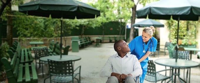 A person in a wheelchair having a conversation with another person outdoors.