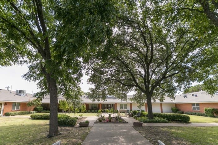 A serene front view of a house surrounded by large trees and a landscaped yard.