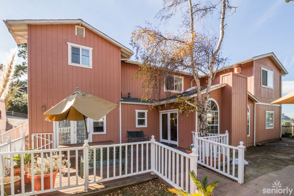 A two-story residential house with a fenced backyard deck and trees.