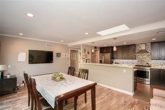 A modern dining area with wood flooring and an open layout leading to the kitchen, featuring a skylight for natural light.