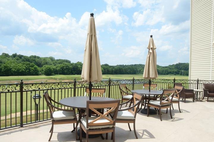 A scenic patio with tables, chairs, and umbrellas overlooking a lush green landscape under a partly cloudy sky.