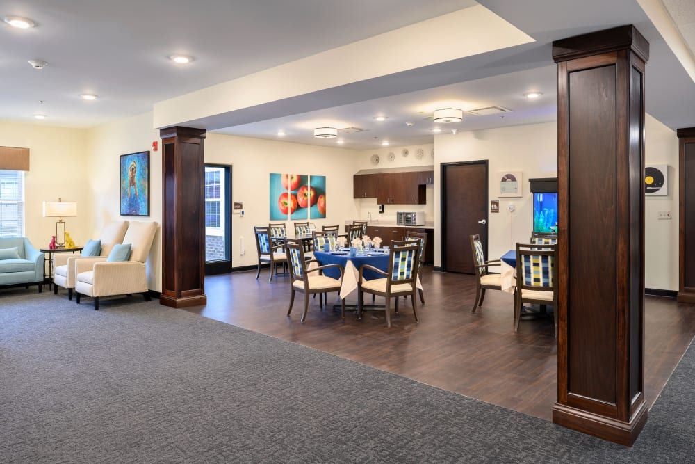 A modern dining area with a kitchen, featuring stylish tables and chairs, enhanced by vibrant artwork and elegant lighting.