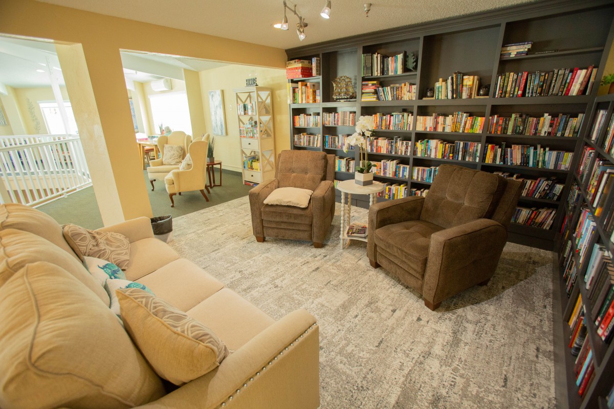 A cozy living room with a bookshelf, chairs, and a couch.