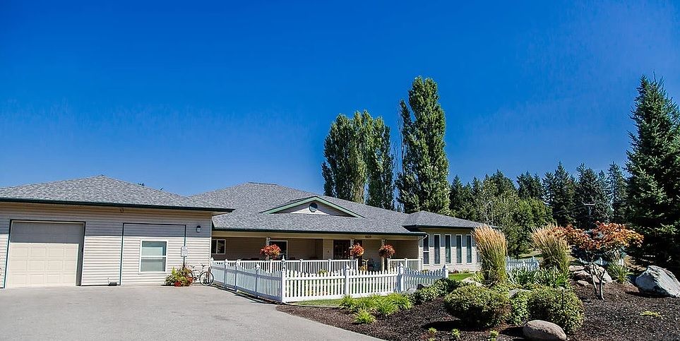 A single-story house with a white fence, surrounded by trees under a clear blue sky.