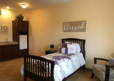 A cozy bedroom with a single bed, featuring decorative pillows and a wall art piece reading 'Blessed'.