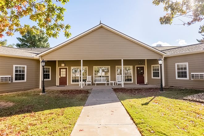 A front view of a residential building with a porch and lawn on a sunny day.
