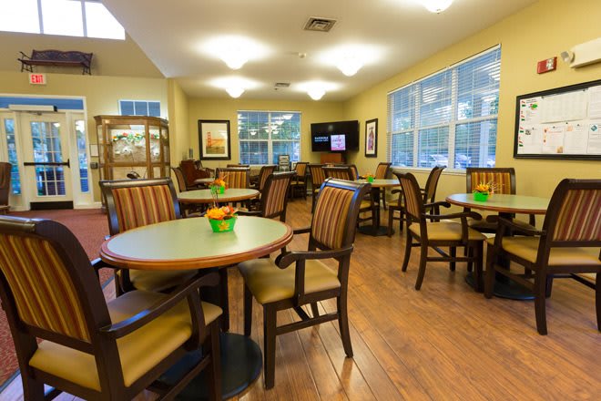 A cozy dining area with several tables and chairs, well-lit by overhead lights and large windows.