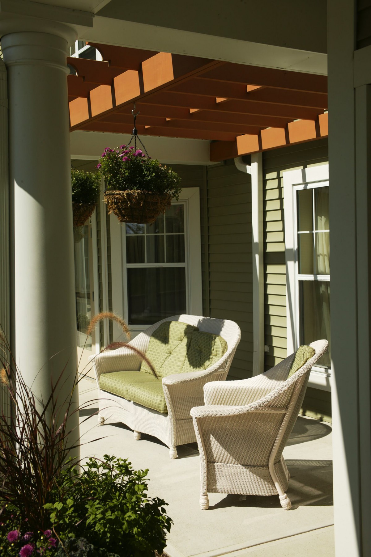 A cozy outdoor patio area featuring wicker furniture under a pergola with hanging plants.