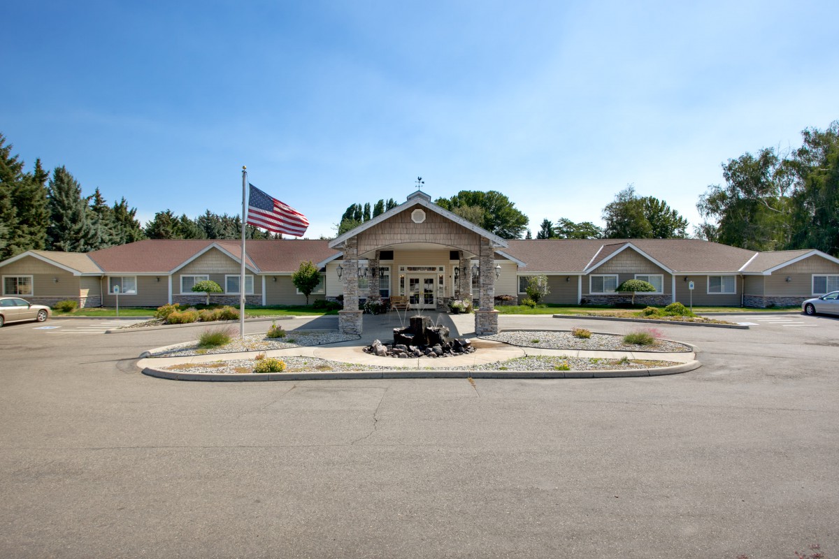 A view of a building entrance with an American flag displayed prominently, surrounded by well-maintained landscaping.