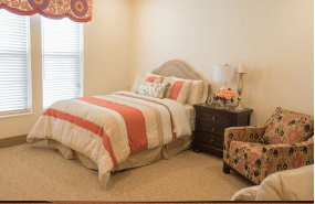 A cozy bedroom with a striped bedspread, nightstand with a lamp, and an accent chair.