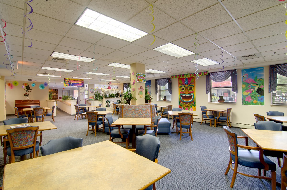 A spacious cafeteria with tables and chairs arranged for casual dining, featuring artwork on the walls and bright overhead lighting.