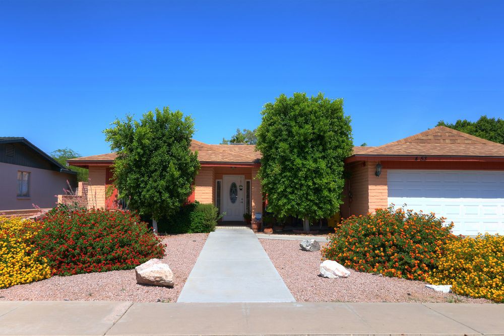 A single-story house with desert landscaping and a clear blue sky.