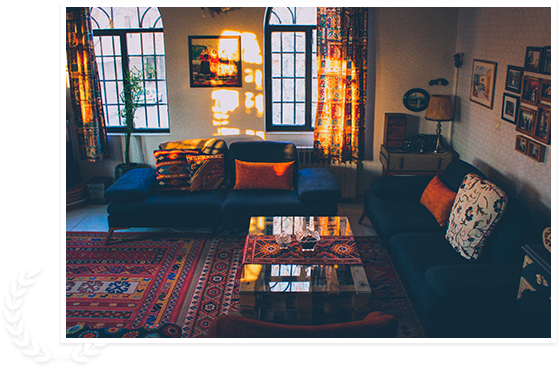A cozy living room bathed in warm sunset light, featuring a dark sofa with colorful throw pillows, a patterned carpet, and a stylish coffee table.