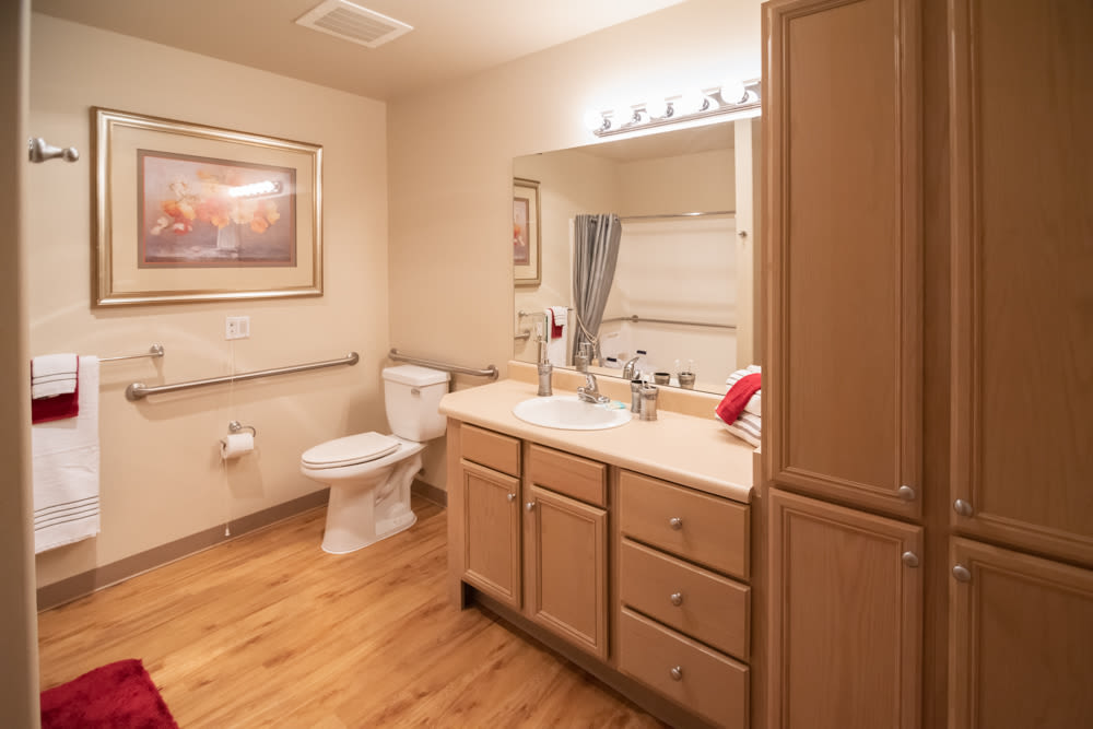 A clean and well-lit bathroom with a wooden cabinet, sink, mirror, and toilet.