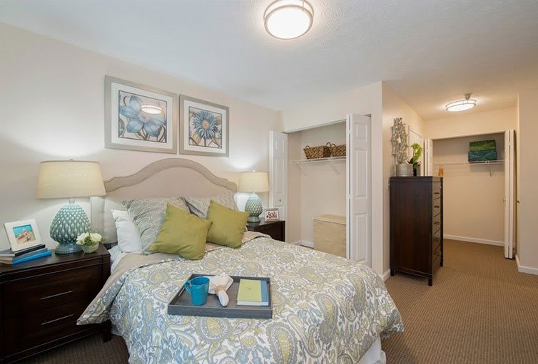 A cozy bedroom with stylish decor, featuring a neatly made bed, artwork above the headboard, and a small closet.