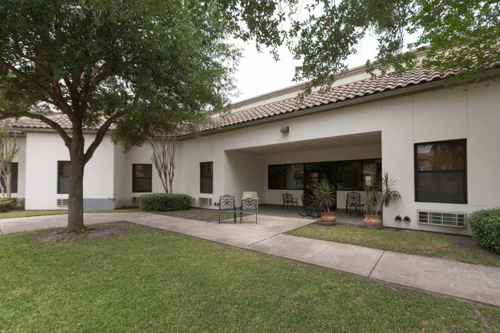 A single-story building with a covered entrance, surrounded by a green lawn and trees.