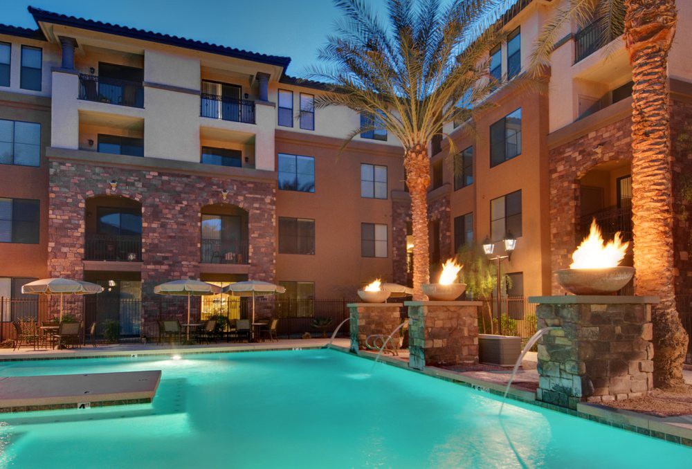 An apartment complex with a beautifully lit swimming pool in the evening.