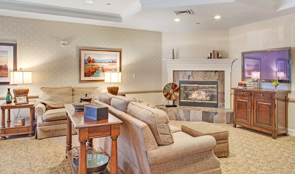 A cozy living room with a comfortable sofa facing a warm fireplace, adorned with artwork and a table lamp.