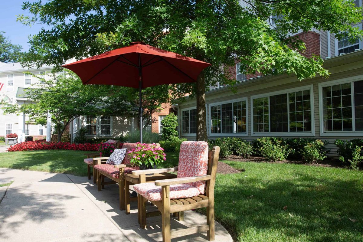 A serene outdoor patio area with wooden chairs and a red umbrella, surrounded by greenery.