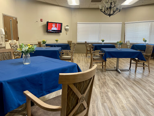A spacious dining room featuring blue tablecloths, wooden chairs, and a television on the wall.
