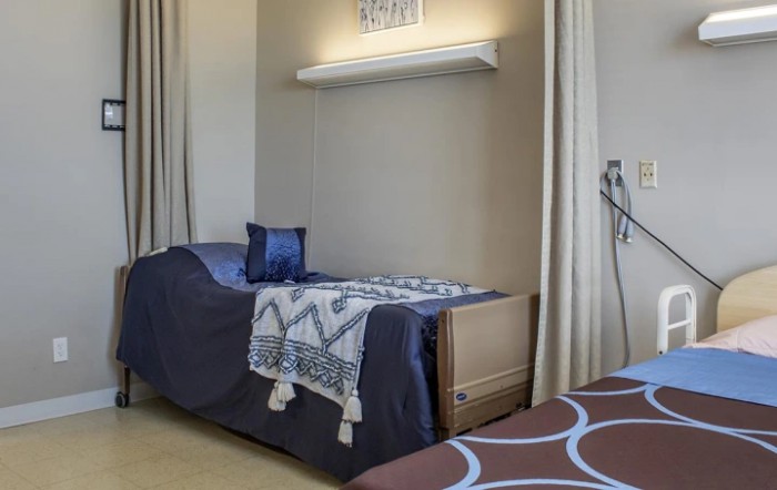 A cozy bedroom with a single bed, adorned with a patterned blanket and pillow, featuring a modern lamp.
