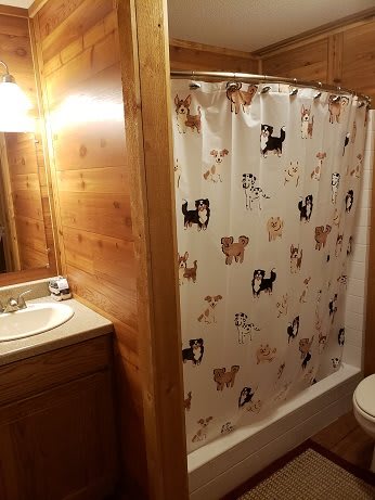 A cozy bathroom with wood paneling and a dog-themed shower curtain.