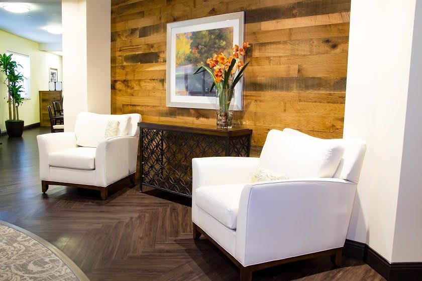 A modern living room with white chairs, a wooden accent wall, and vibrant floral decor.