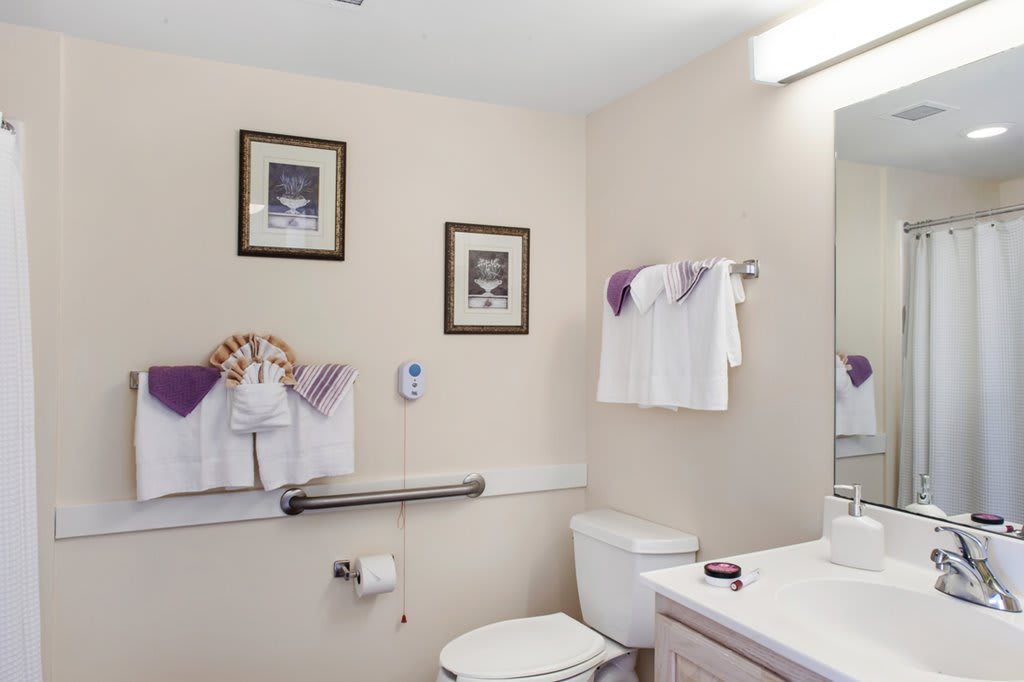 A neatly arranged bathroom featuring a toilet, sink, mirror, and towels with decorative wall art.